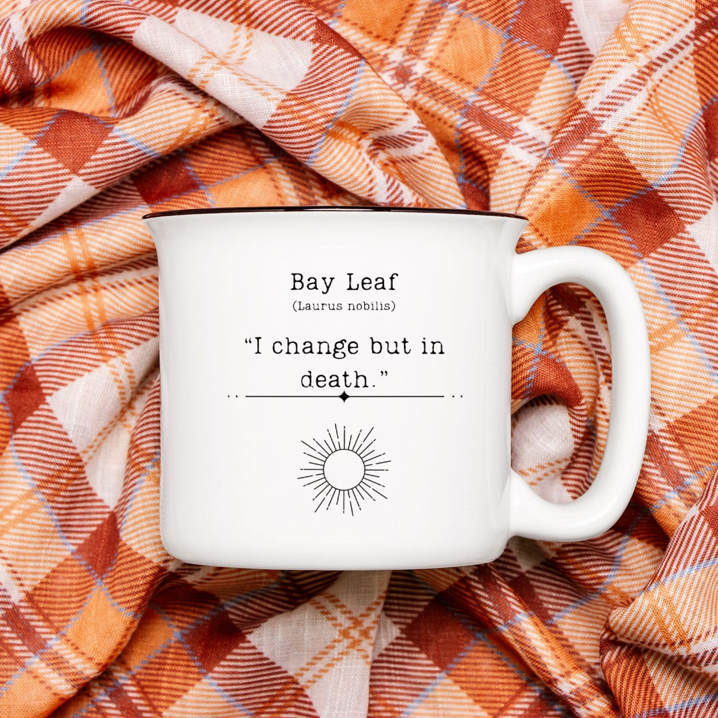 The back view of a white ceramic camp mug with a black rim. Text on the mug reads Bay Leaf (Laurus nobilis) "I change but in death." The text is printed over a black outline of a sun.