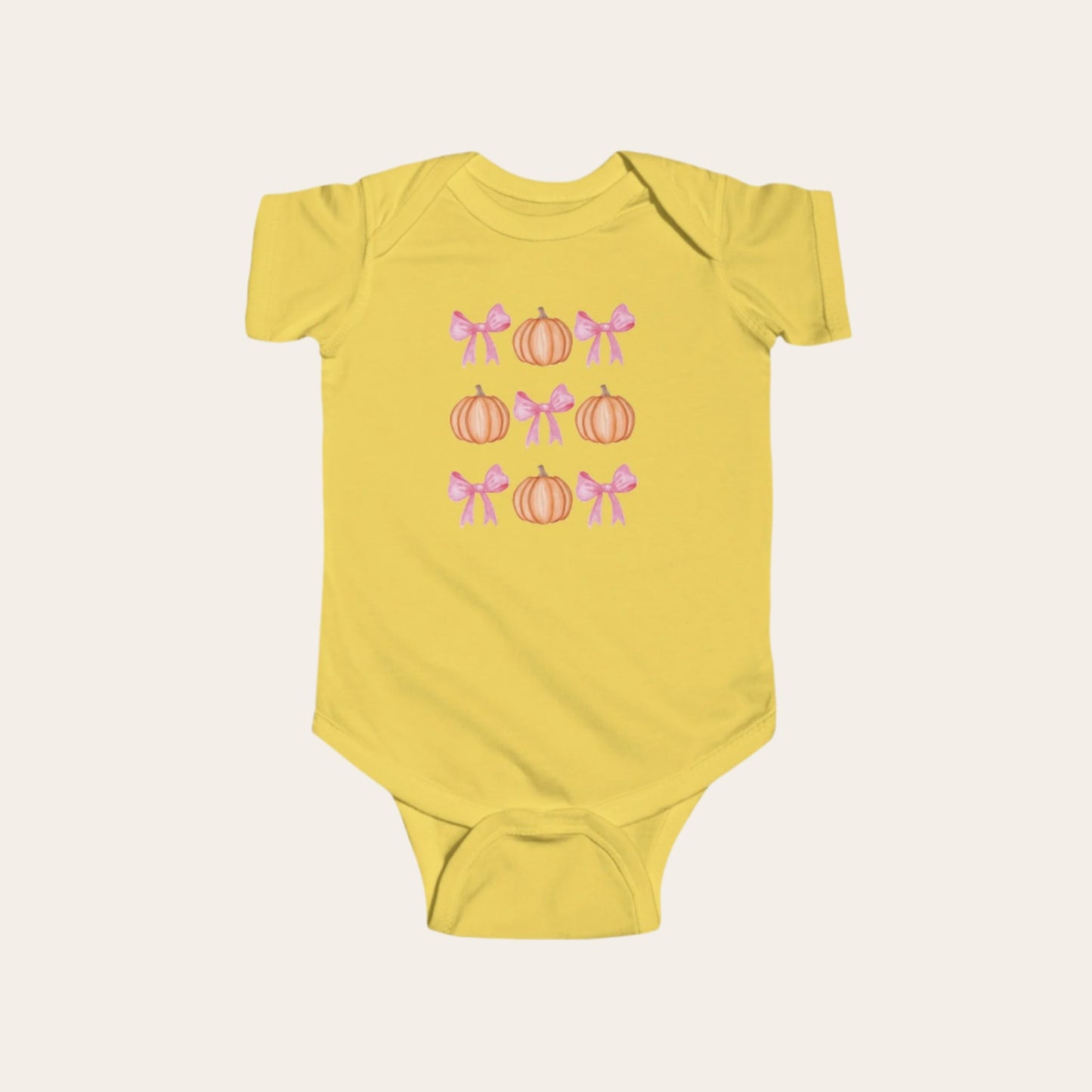 A deep yellow, infant onesie with a pattern of alternating pink bows and orange pumpkins.