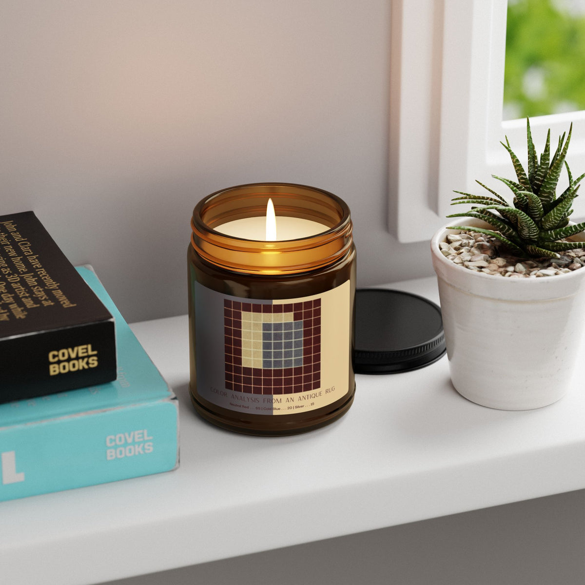 Amber glass candle jar with a black lid and a label showing a ten-by-ten grid of deep red squares surrounding a block of slate blue and a pale cream section, titled Color Analysis from an Antique Rug.