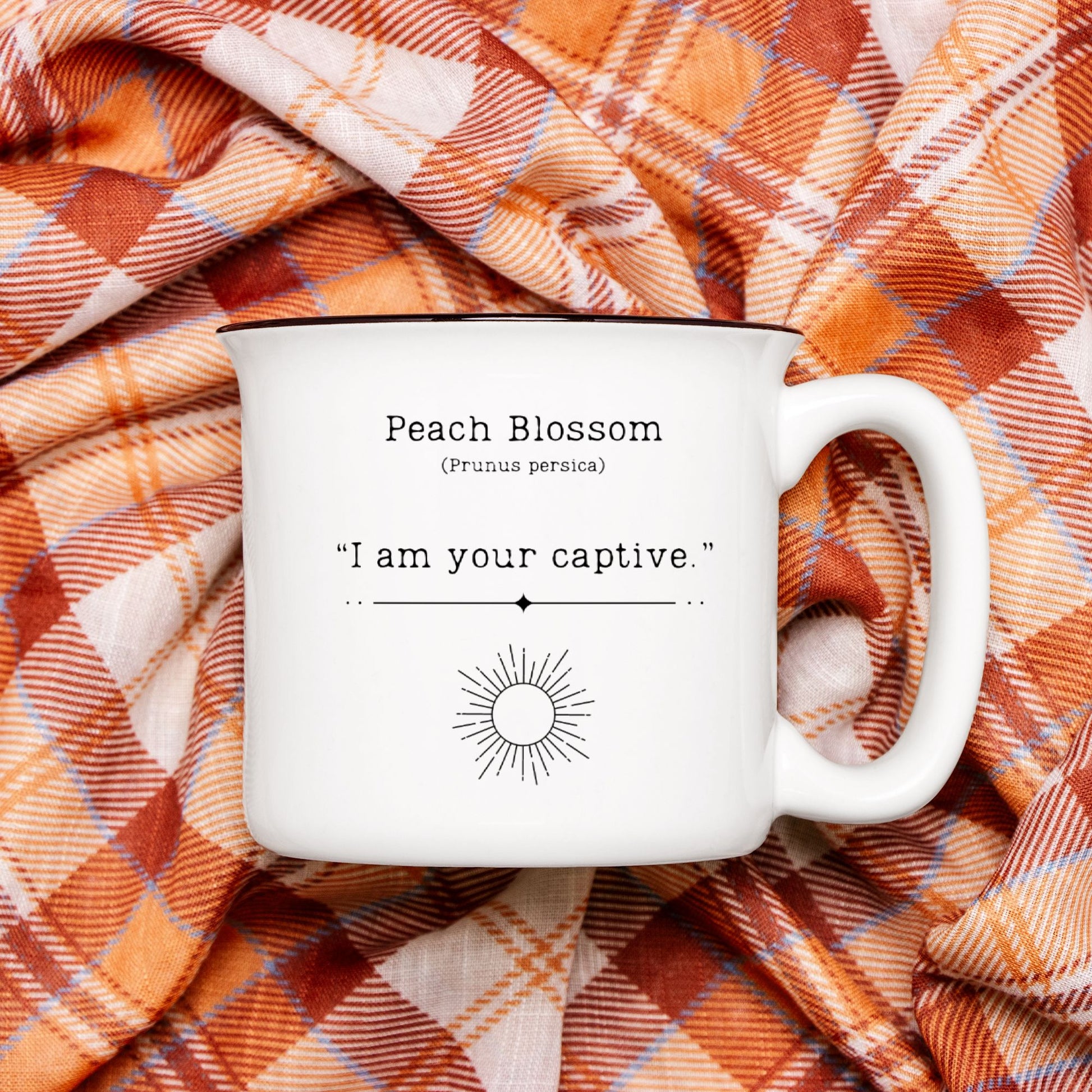 The back view of a black ceramic camp mug with a black rim. Text on the mug reads Peach Blossom (Prunus persica) "I am your captive". The text is printed above a black outline of a sun.