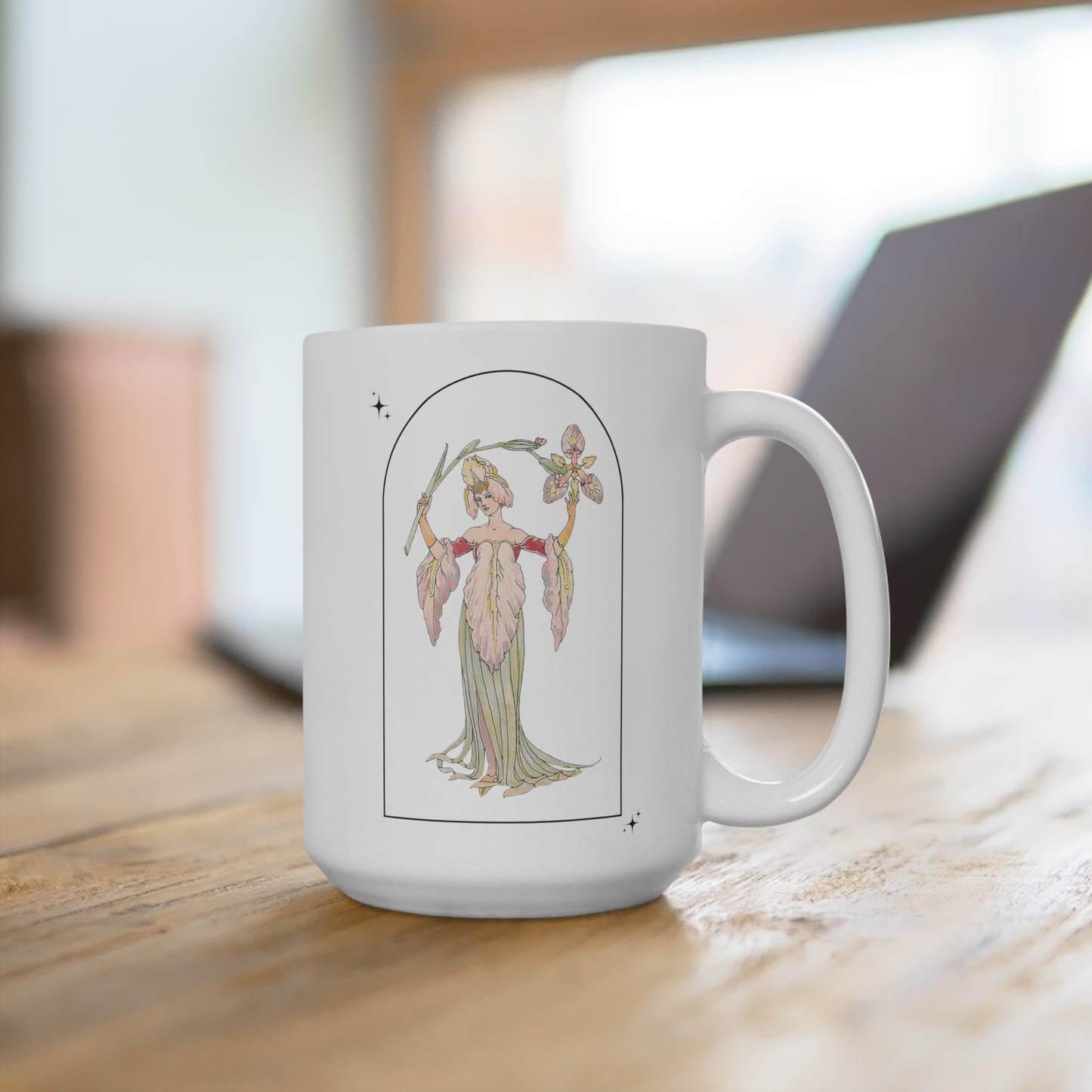 A white mug featuring a vintage illustration of a woman wearing a dress and crown made of lilies. The woman holds a lily over her head, in an arched shape. The mug sits on a wooden table with a blurry laptop in the background.