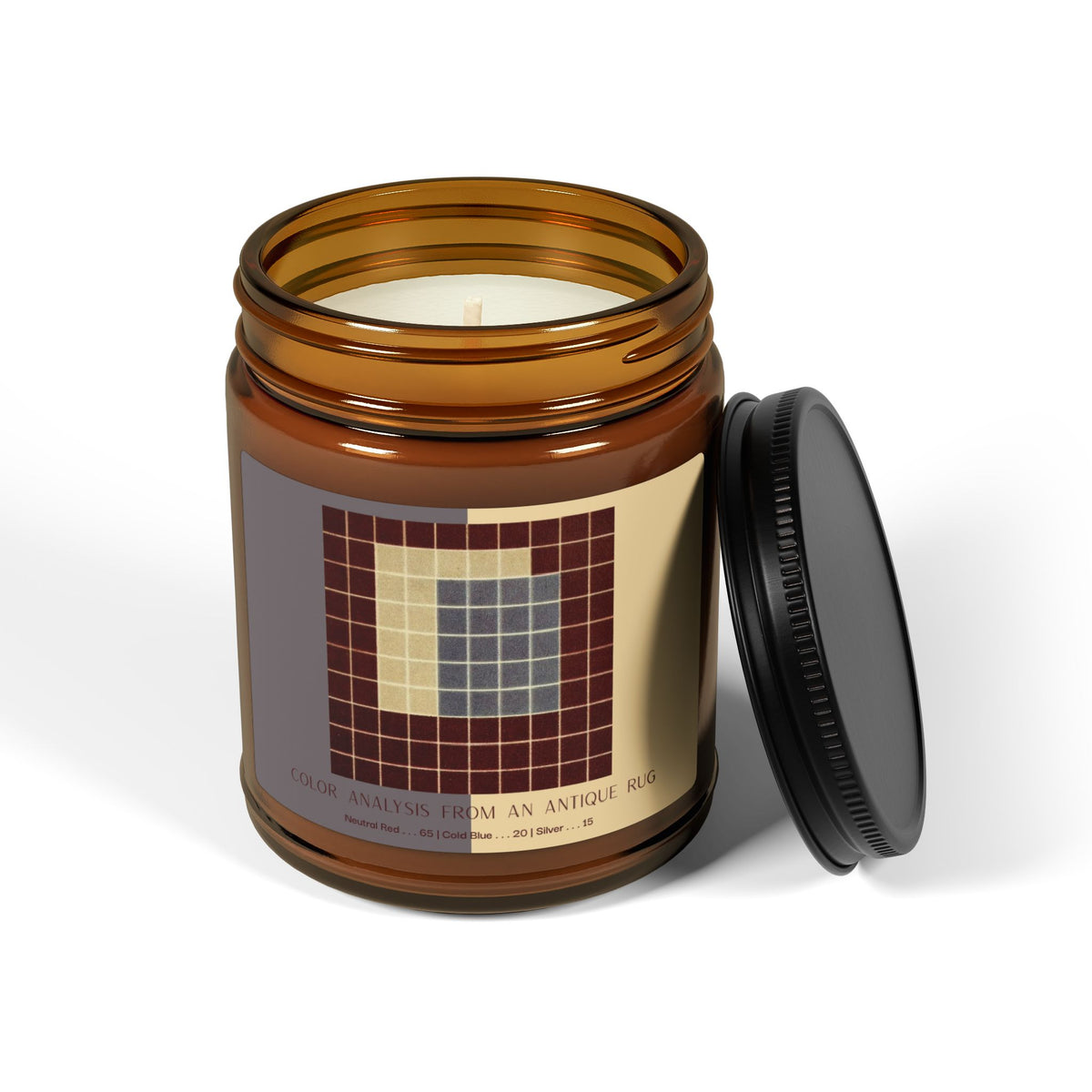 Amber glass candle jar with a black lid and a label showing a ten-by-ten grid of deep red squares surrounding a block of slate blue and a pale cream section, titled Color Analysis from an Antique Rug.