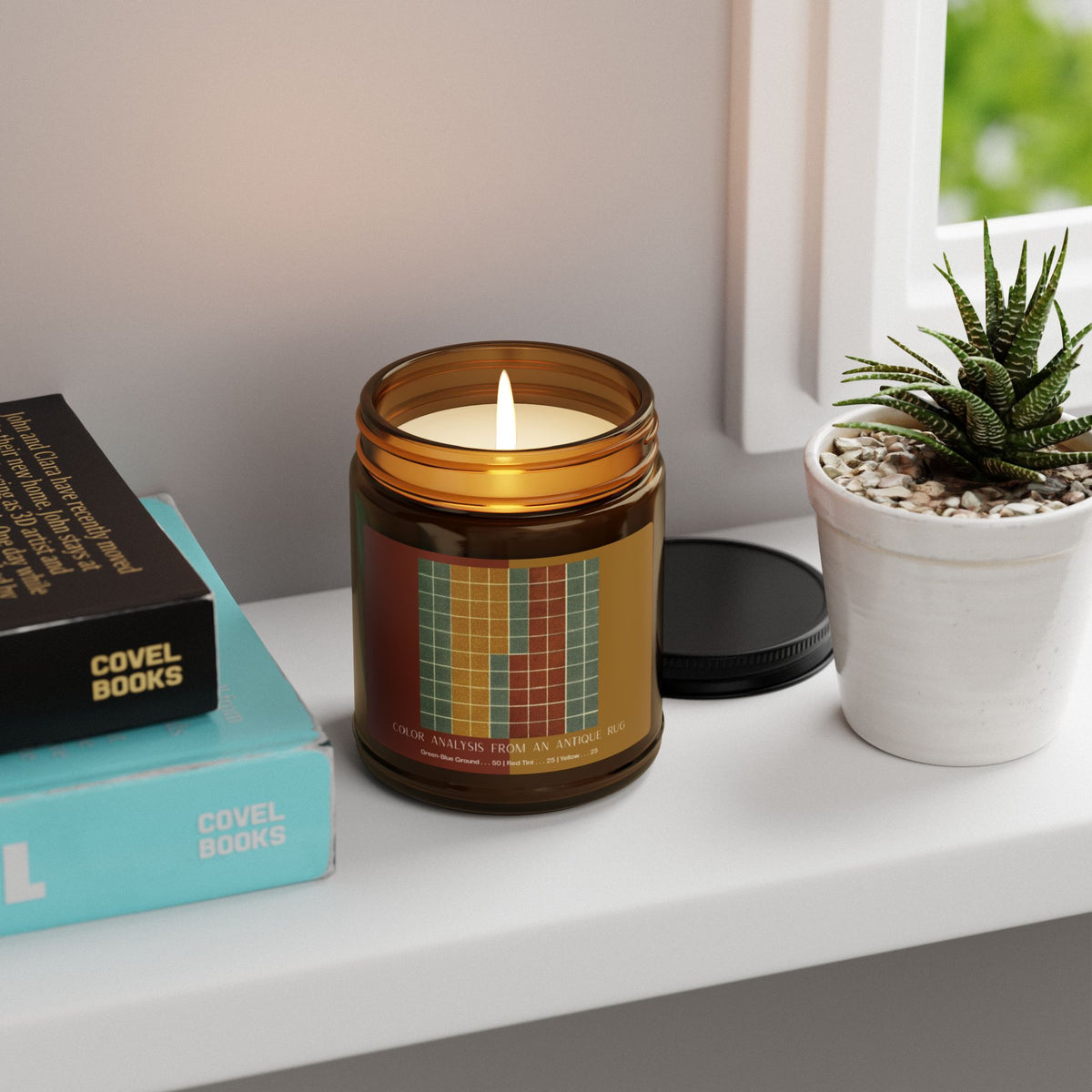 Amber glass candle jar with a black lid and a label showing a ten-by-ten grid of gray-green squares with vertical bands of golden yellow and brick red, titled Color Analysis from an Antique Rug.