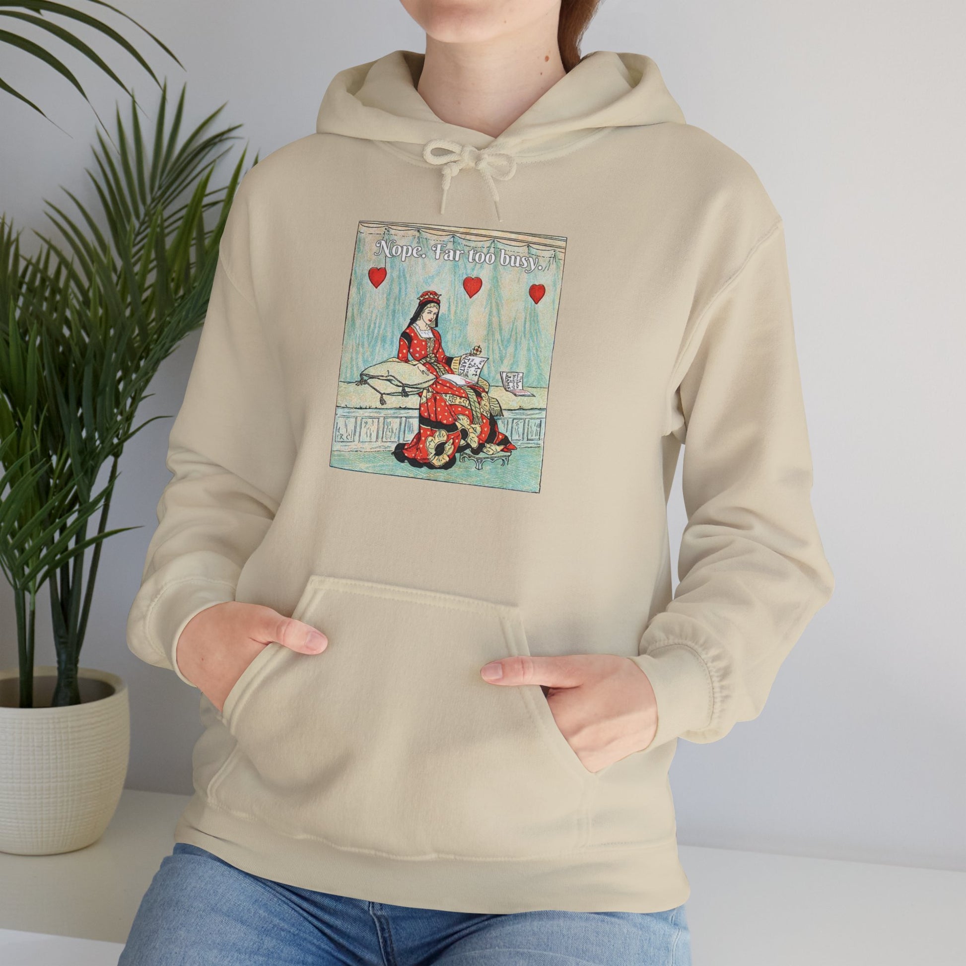 A woman wears a beige hoodie with a vintage illustration of the Queen of Hearts lounging on a bench reading The Art of Making Tarts. Above her the text reads "Nope. Far too busy."