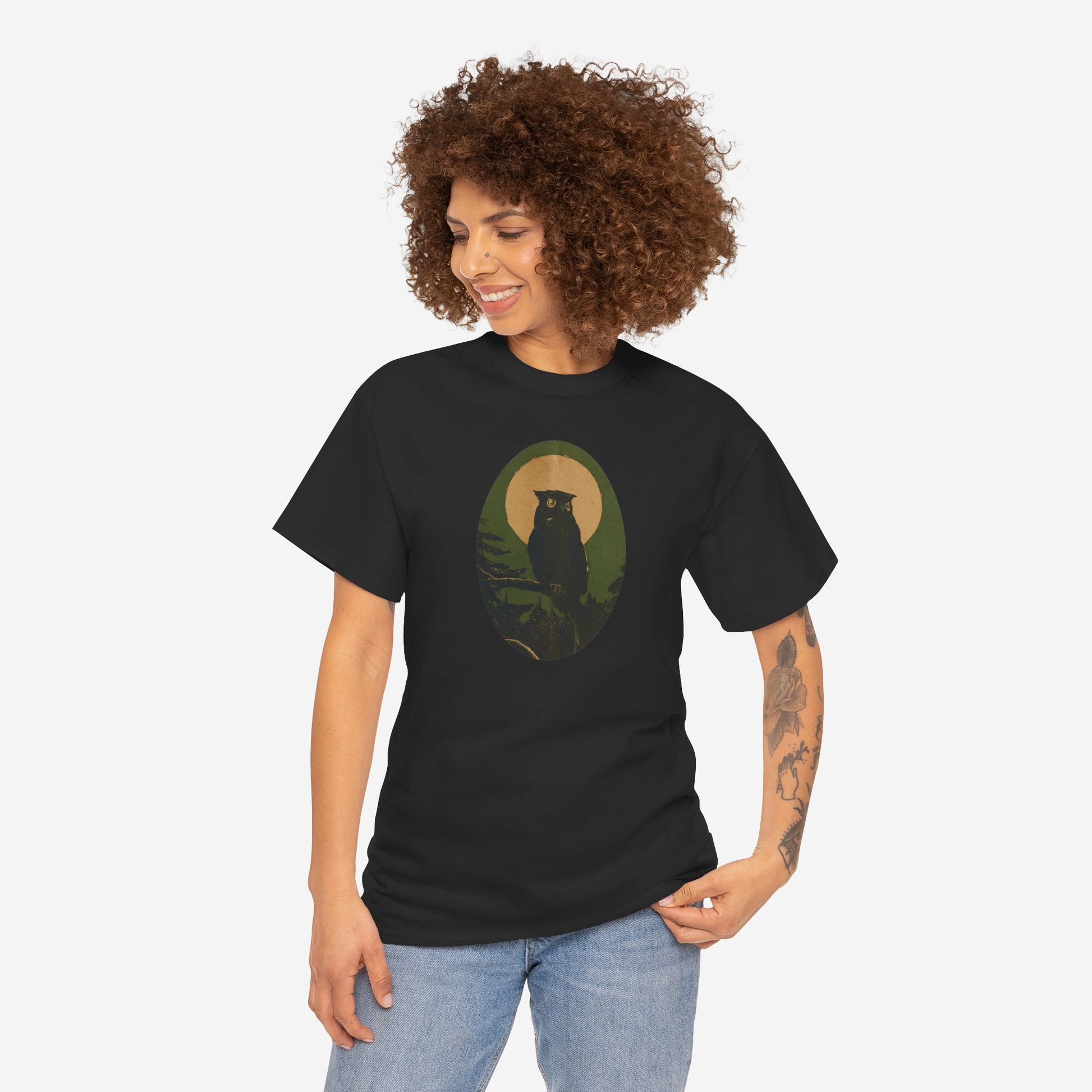 A woman wears a black t shirt featuring an image of an owl on a branch with the full moon behind it. The image is colored in yellow, green, and black.