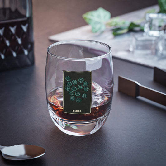 Clear whiskey glass displaying a dark rectangular plate with a scattered cluster of small turquoise woodblock firework bursts.