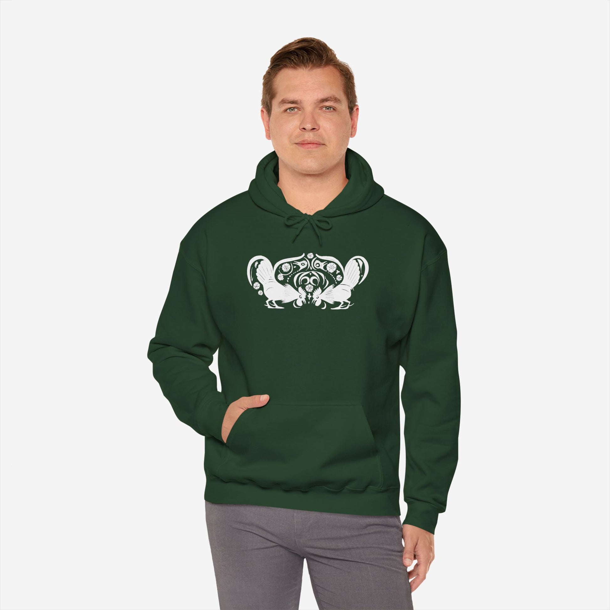 A man wears a forest green hoodie with a white, art noveau style print of two roosters crouching face-to-face. The roosters are mirror images of each other and a symmetrical pattern arches between them.