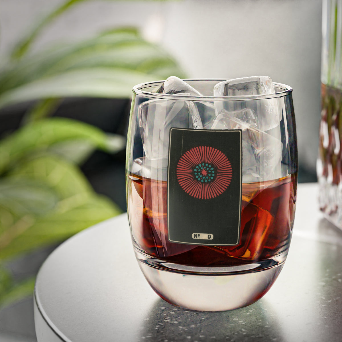 Clear whiskey glass displaying a dark rectangular plate with a crimson and turquoise sunburst woodblock firework print.