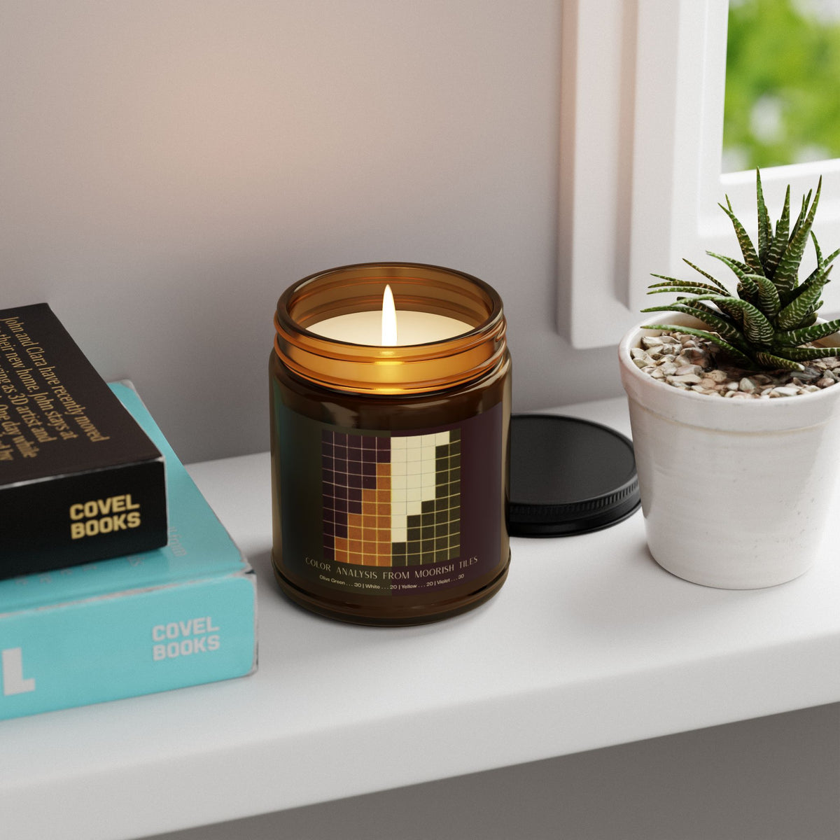 Amber glass candle jar with a black lid and a label showing a ten-by-ten grid of violet, golden yellow, cream, and olive green squares, titled Color Analysis from Moorish Tiles.