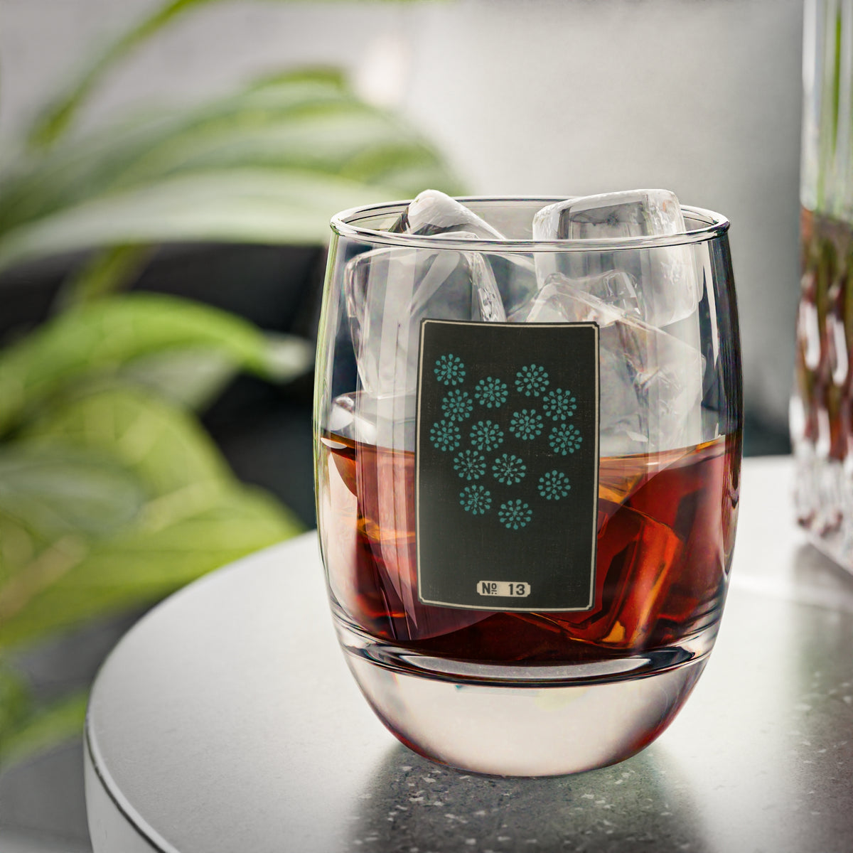 Clear whiskey glass displaying a dark rectangular plate with a scattered cluster of small turquoise woodblock firework bursts.