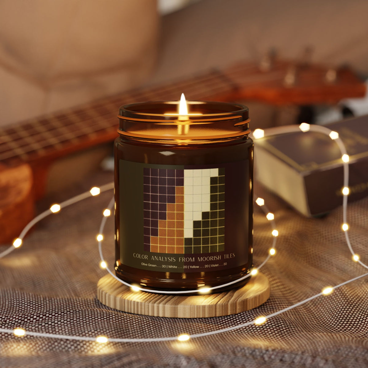 Amber glass candle jar with a black lid and a label showing a ten-by-ten grid of violet, golden yellow, cream, and olive green squares, titled Color Analysis from Moorish Tiles.