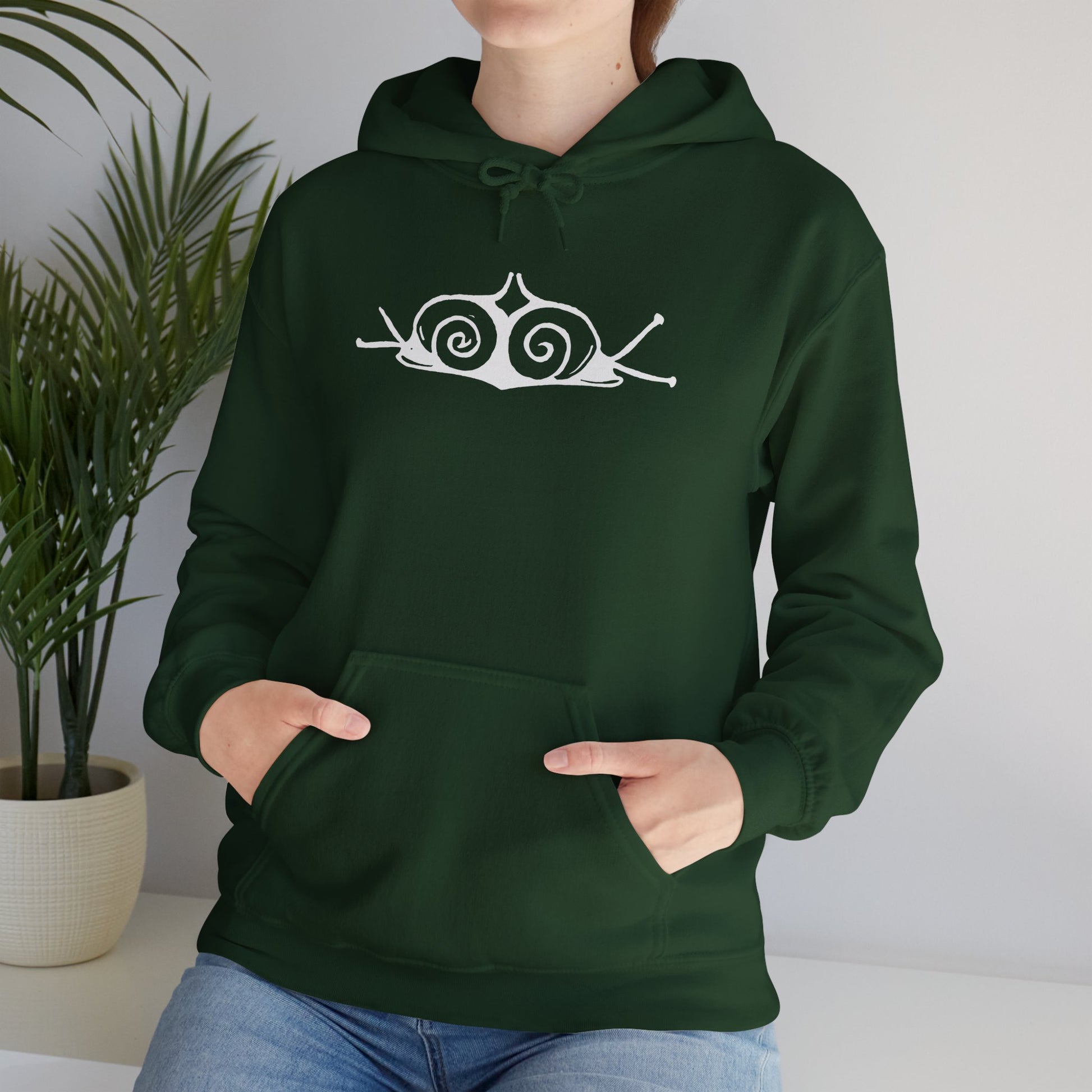 A woman wears a forest green hoodie with a white, art noveau style print of two snails facing away from each other. The snails are mirror images of each other and slightly overlap in the middle of the design.