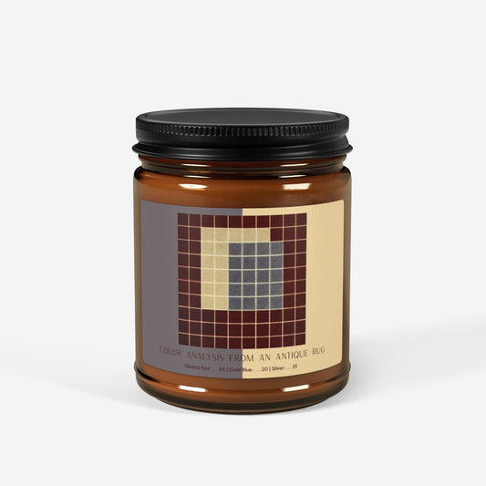 Amber glass candle jar with a black lid and a label showing a ten-by-ten grid of deep red squares surrounding a block of slate blue and a pale cream section, titled Color Analysis from an Antique Rug.
