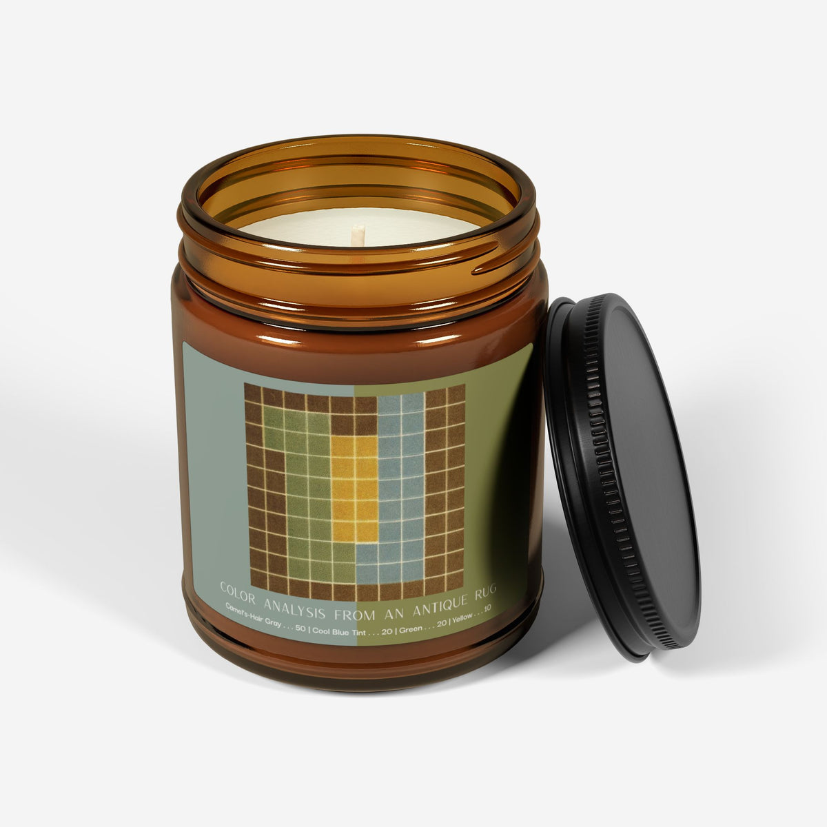 Amber glass candle jar with a black lid and a label showing a ten-by-ten grid with a camel-brown border around columns of sage green, pale blue, and yellow, titled Color Analysis from an Antique Rug.