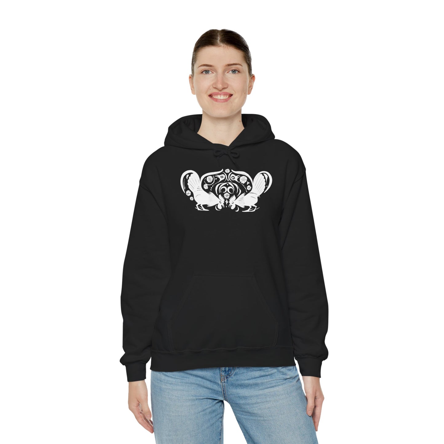 A woman wears a black hoodie with a white, art noveau style print of two roosters crouching face-to-face. The roosters are mirror images of each other and a symmetrical pattern arches between them.