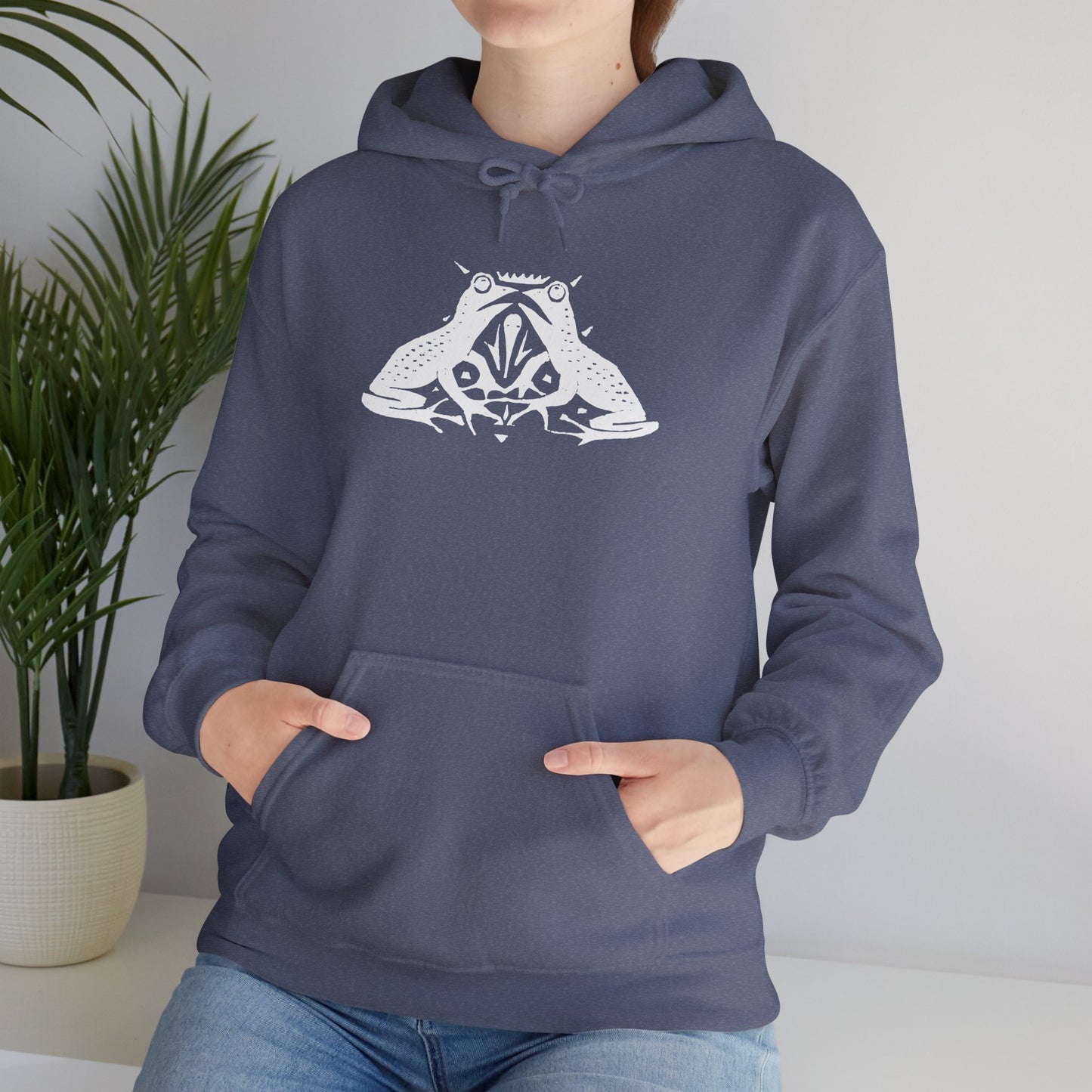 A woman wears a heather navy hoodie with a white, art noveau style print of two frogs facing each other. The frogs are mirror images of each other.