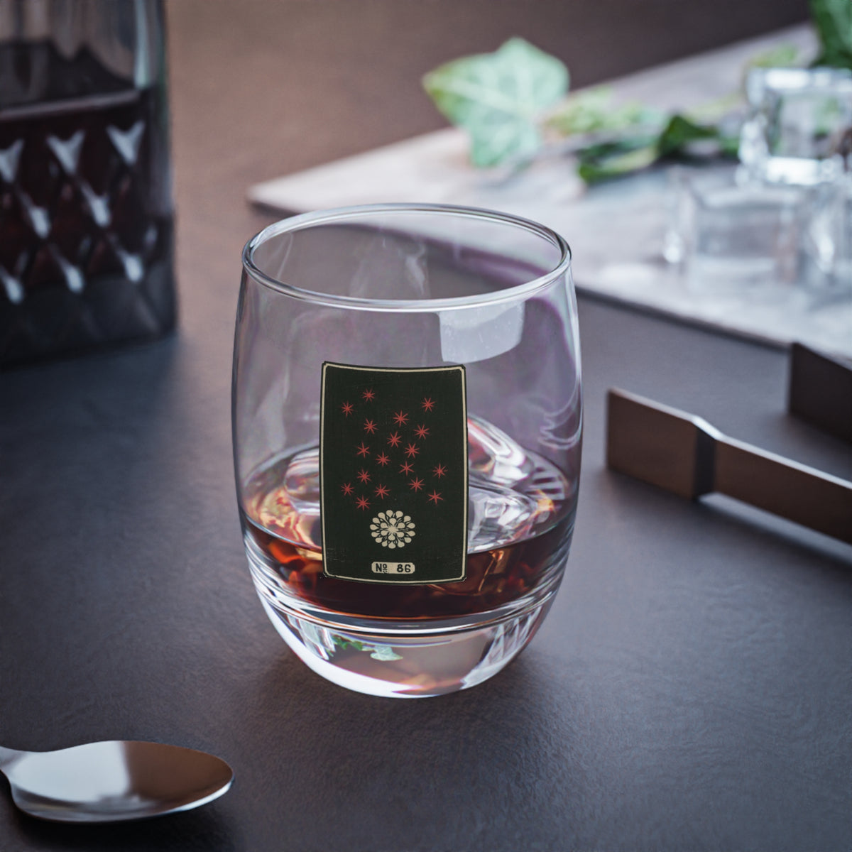 Clear whiskey glass displaying a dark rectangular plate with an ivory burst and rising red stars woodblock firework print.
