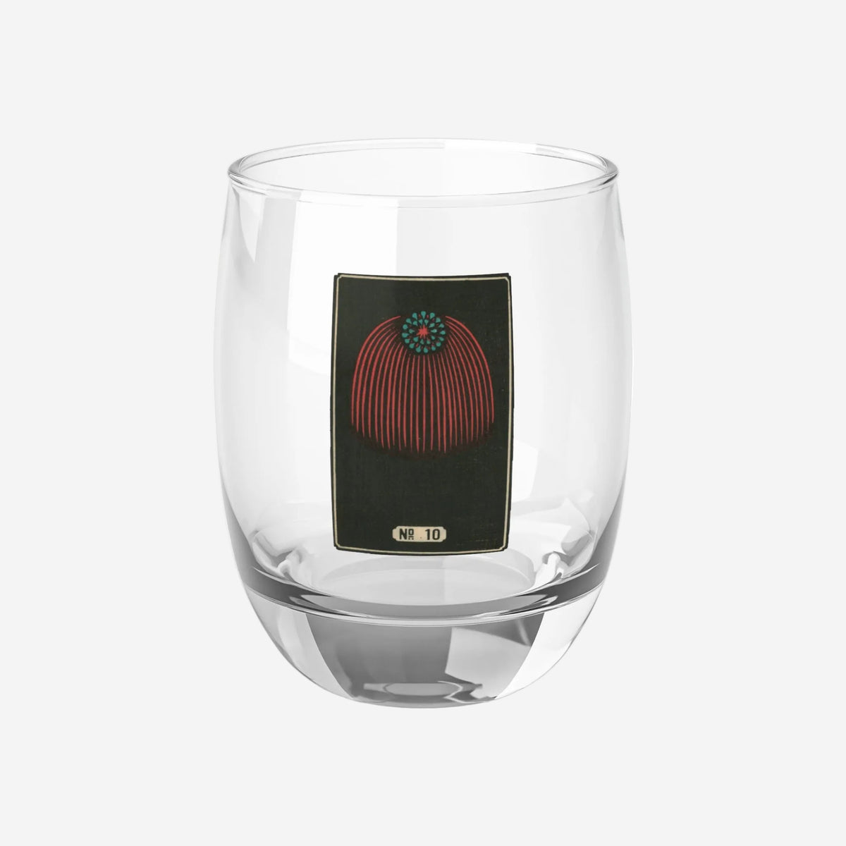 Clear whiskey glass displaying a dark rectangular plate with a crimson and turquoise cascading canopy woodblock firework print.