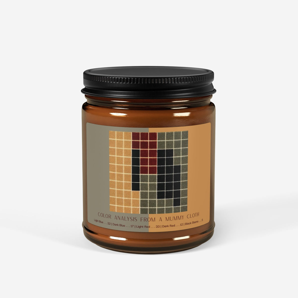 Amber glass candle jar with a black lid and a label showing a ten-by-ten grid of ochre, gray-green, dark red, and black squares, titled Color Analysis from a Mummy Cloth.