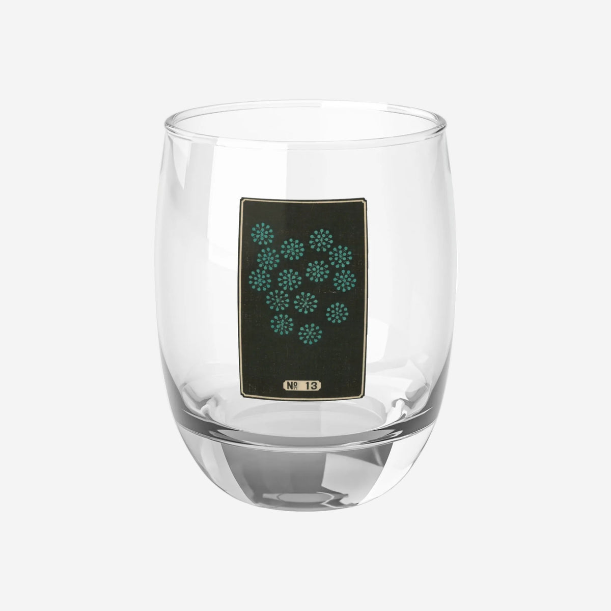 Clear whiskey glass displaying a dark rectangular plate with a scattered cluster of small turquoise woodblock firework bursts.
