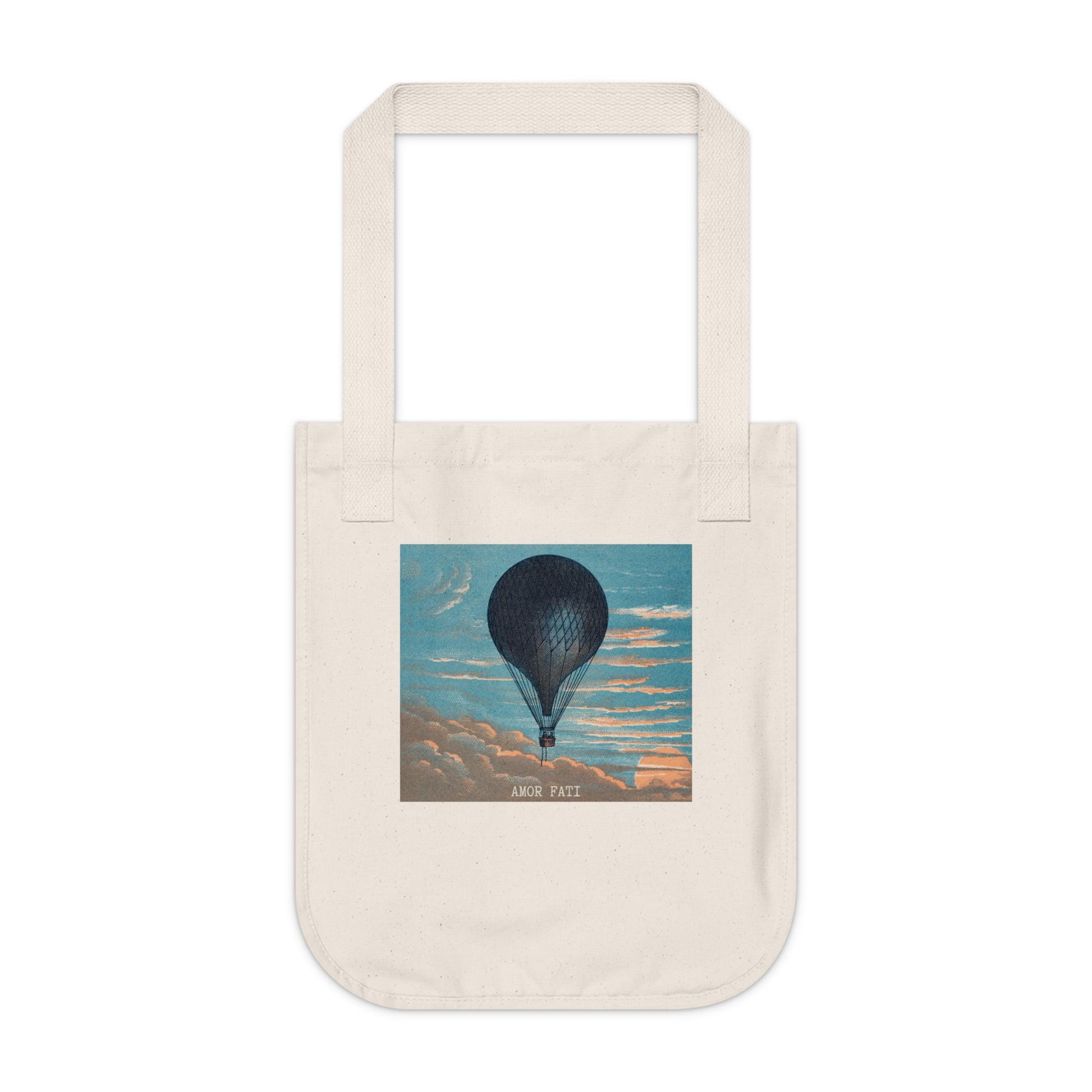Natural canvas tote bag, front view, featuring a dark hot air balloon against a blue sky with peach-toned clouds, with the text "AMOR FATI" beneath.