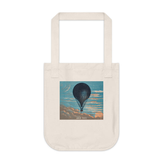 Natural canvas tote bag, front view, featuring a dark hot air balloon against a blue sky with peach-toned clouds, with the text "AMOR FATI" beneath.