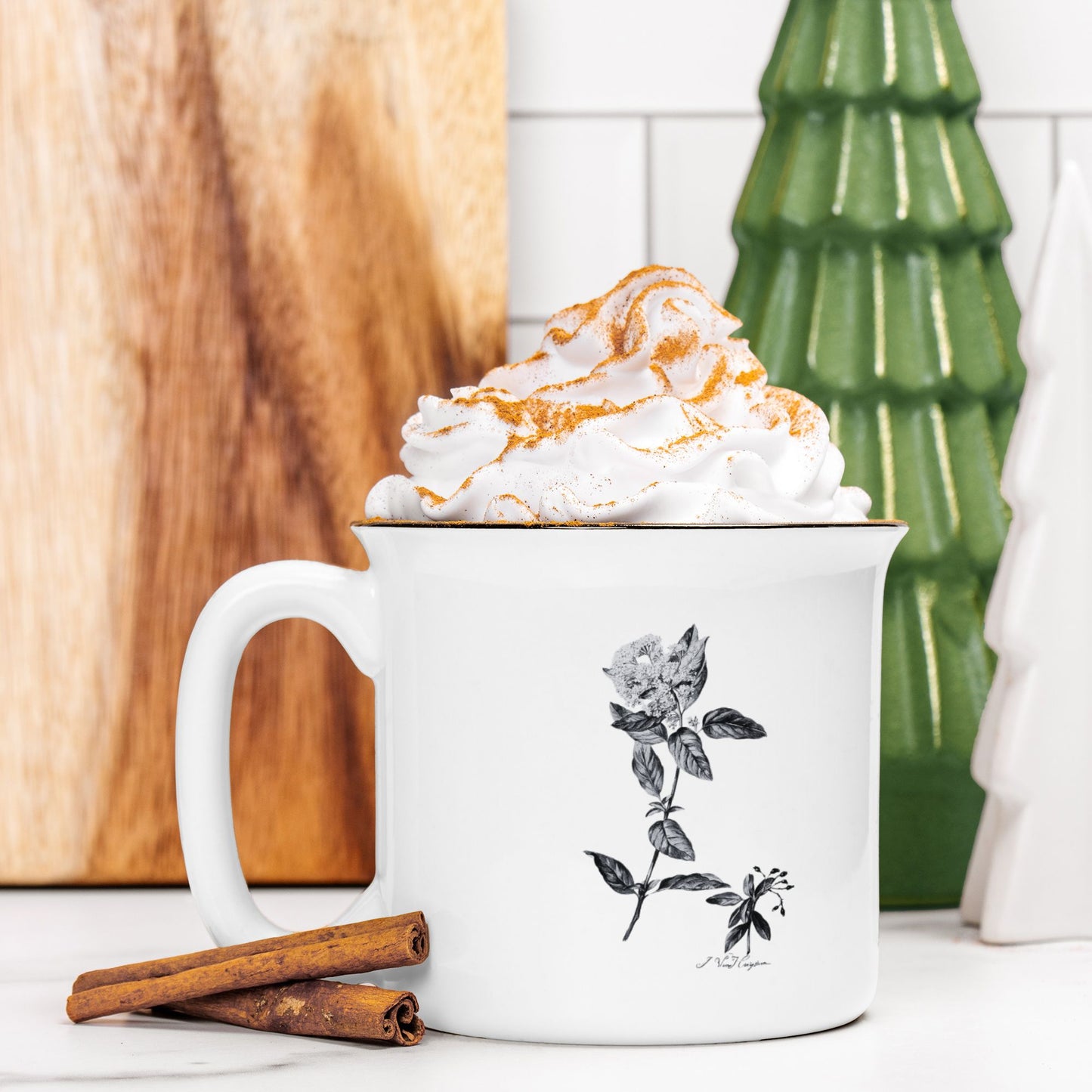 The front view of a white ceramic camp mug with a black rim. The mug features a black and white botanical illustration of a Laurestina flower. The mug is filled and topped with whipped cream and a stick of cinnamon sits next to it.