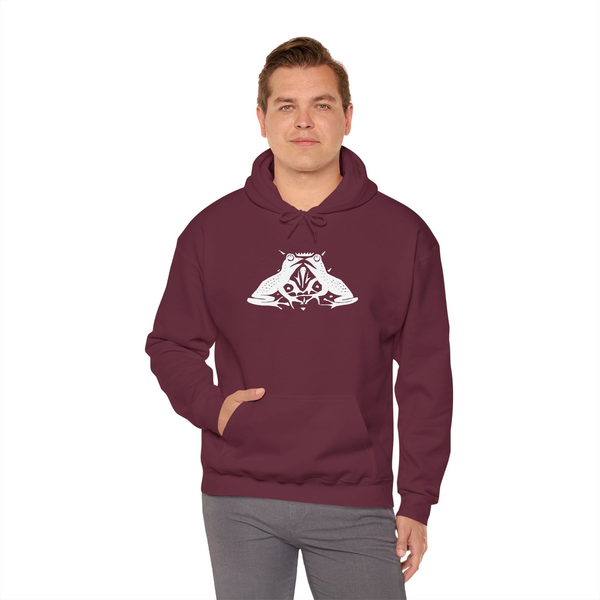 A man wears a maroon hoodie with a white, art noveau style print of two frogs facing each other. The frogs are mirror images of each other.