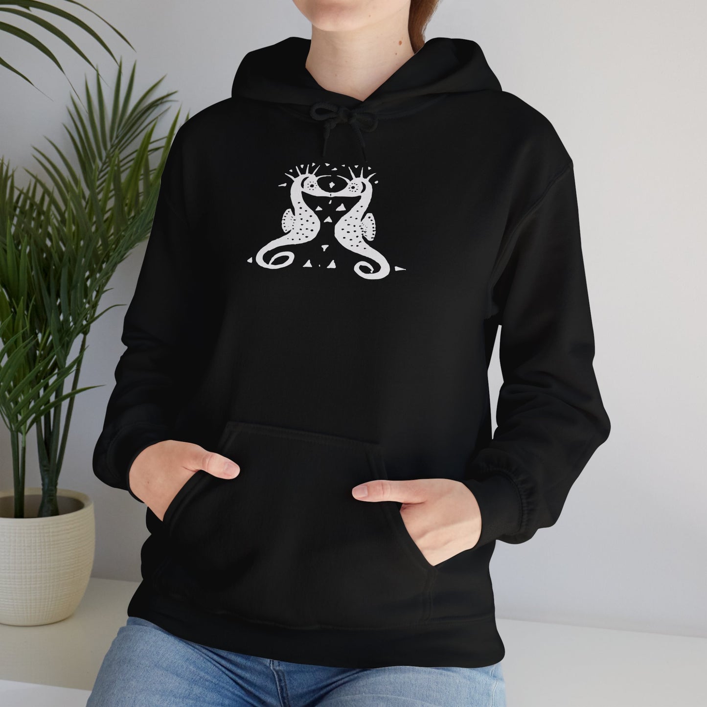 A woman wears a black hoodie with a white, art noveau style print of two seahorses facing each other. The seahorses are mirror images of each other.