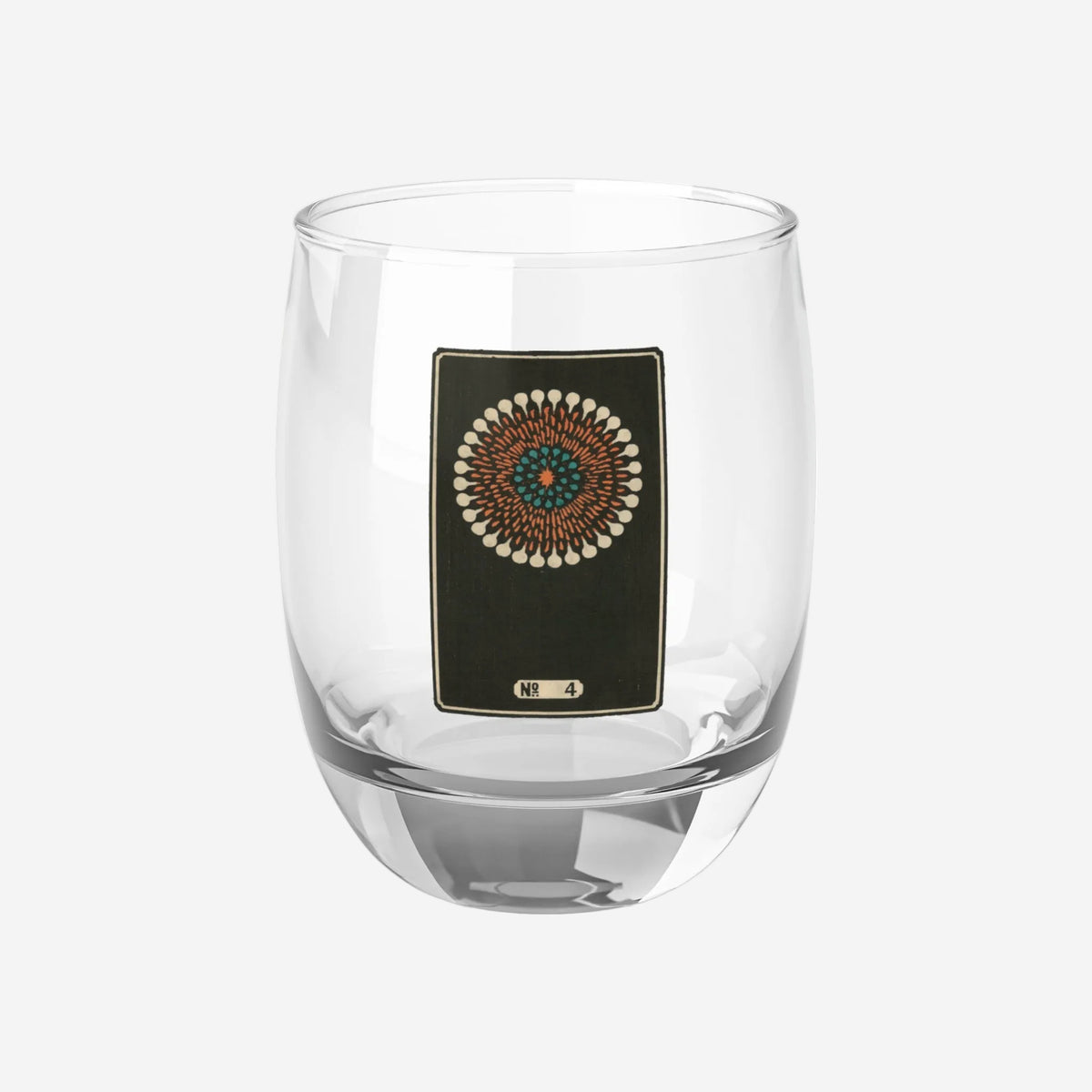 Clear whiskey glass displaying a dark rectangular plate with a cream, orange, and turquoise woodblock firework print.