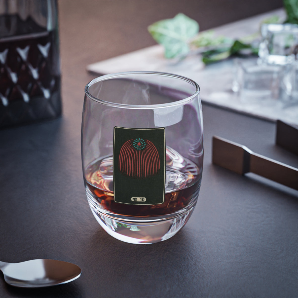 Clear whiskey glass displaying a dark rectangular plate with a crimson and turquoise cascading canopy woodblock firework print.