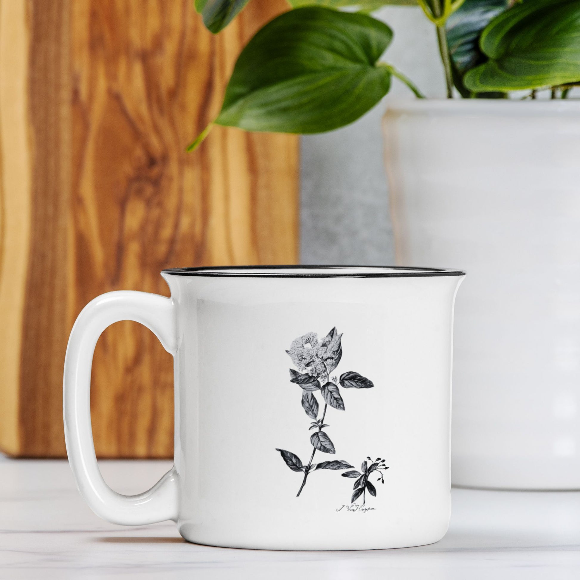 The front view of a white ceramic camp mug with a black rim. The mug features a black and white botanical illustration of a Laurestina flower.